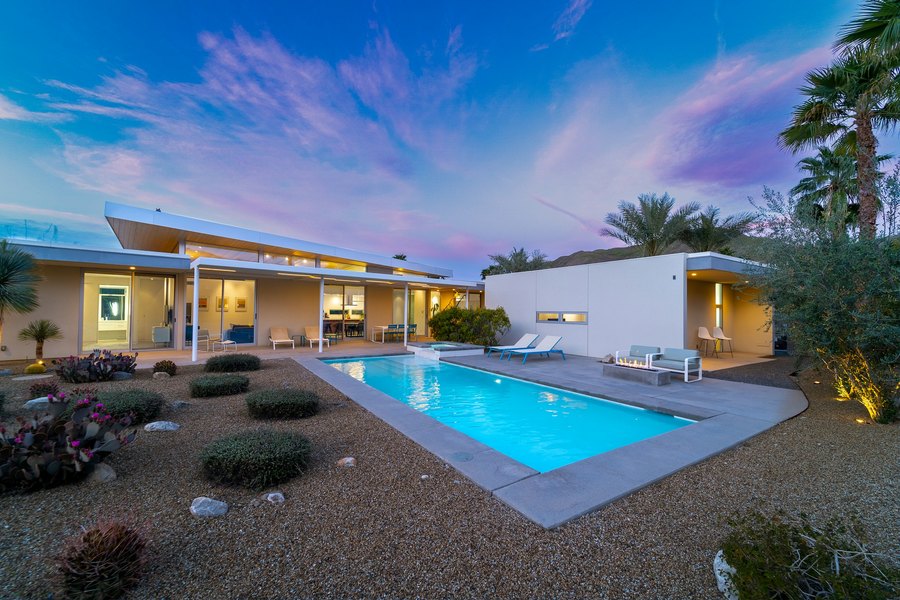 Modern estate and lit pool under a pink and violet twilight sky